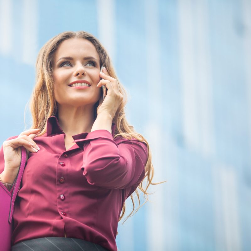 Middle-aged businesswoman smiling and communicating with her partners. Young attractive smiling woman speaking over cell phone in the city.